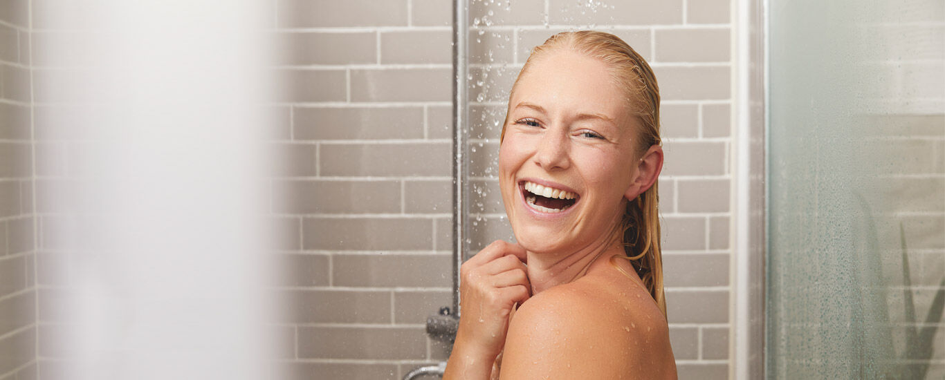 Blonde Frau steht lachend unter der Dusche 
